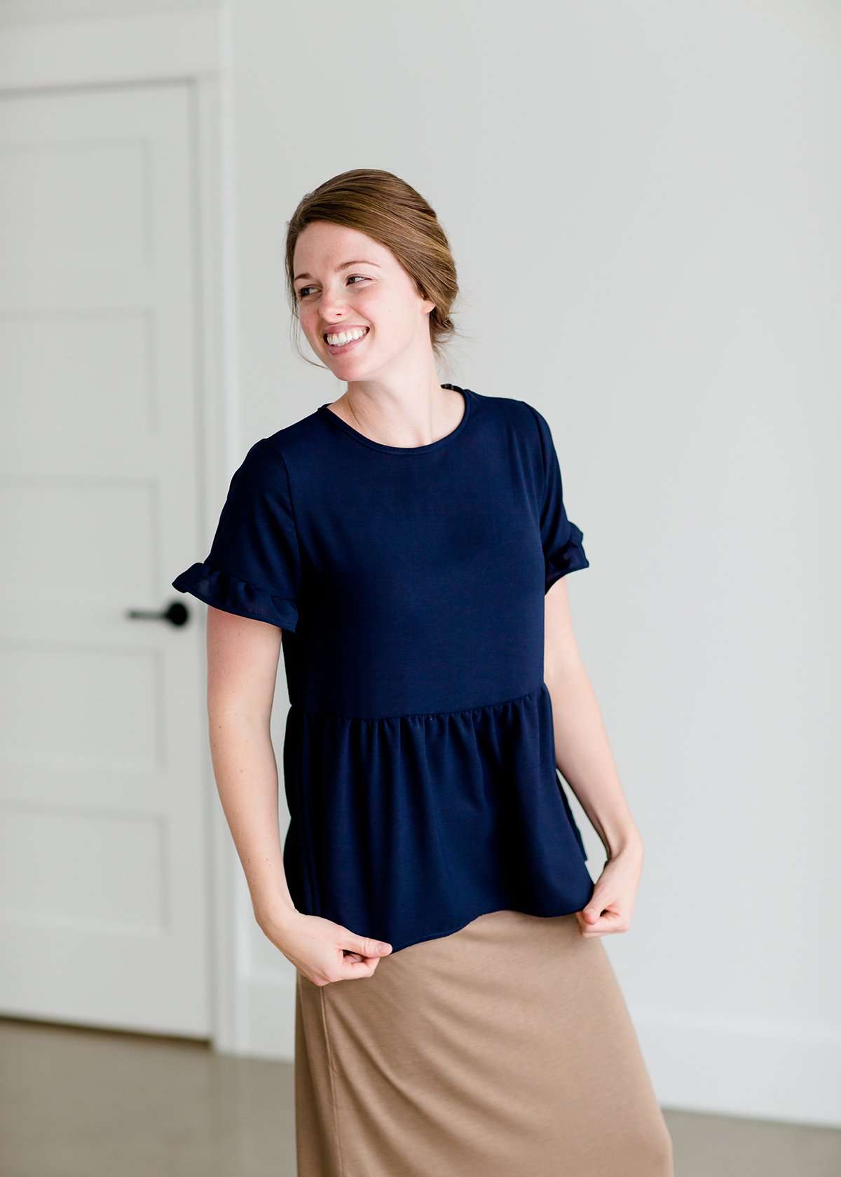 Woman wearing a navy peplum baby doll top that has ruffle details on the sleeves.