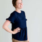 Woman wearing a navy peplum baby doll top that has ruffle details on the sleeves.