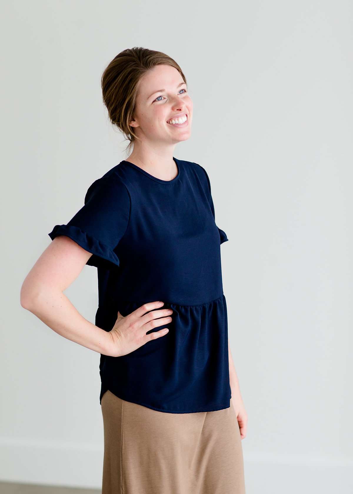 Woman wearing a navy peplum baby doll top that has ruffle details on the sleeves.