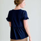 Woman wearing a navy peplum baby doll top that has ruffle details on the sleeves.
